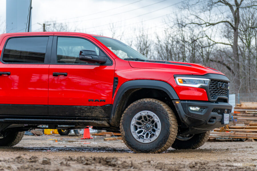 Cropped front quarter view of a red 2025 Ram 1500 RHO, showing the restyled front fascia and wheels, with trees in the background