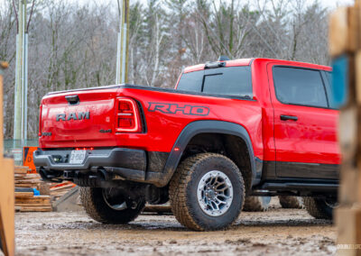 Cropped rear quarter view of a red 2025 Ram 1500 RHO parked in a muddy construction site, with trees in the background