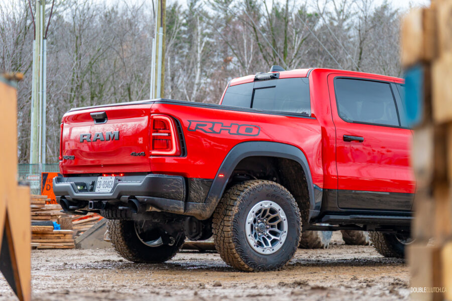 Cropped rear quarter view of a red 2025 Ram 1500 RHO parked in a muddy construction site, with trees in the background