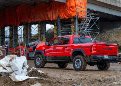 Rear quarter view of a red 2025 Ram 1500 RHO, parked in a muddy construction site