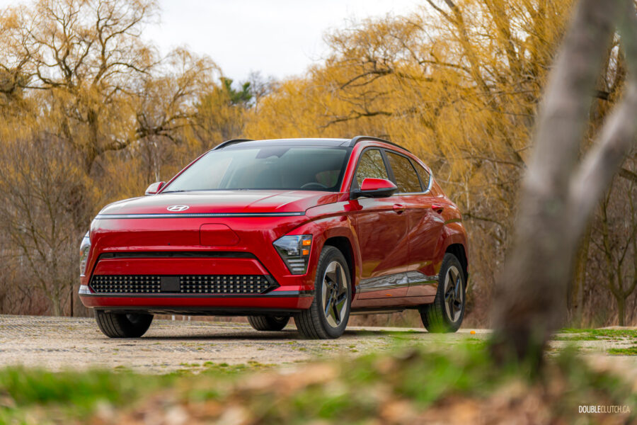 Front quarter view of a red 2025 Hyundai Kona Electric on a cloudy day, with trees in the background