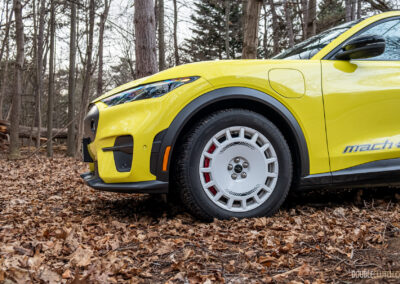 Cropped front quarter view of a yellow 2025 Ford Mustang Mach-E Rally in a forest