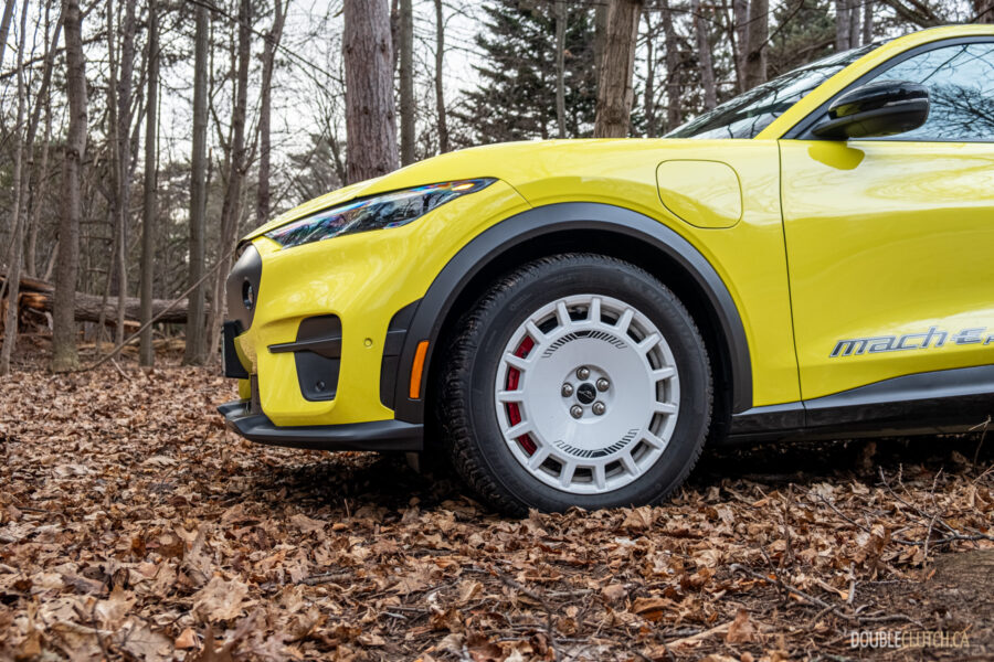 Cropped front quarter view of a yellow 2025 Ford Mustang Mach-E Rally in a forest
